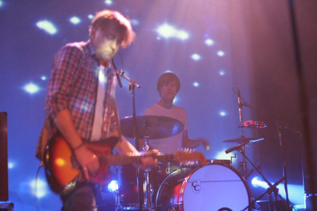 A band playing on a lit stage, seen from among the audience.